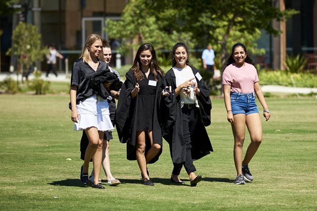 Two girls in academic gowns and three girls in plain clothes walking towards the camera, smiling.
