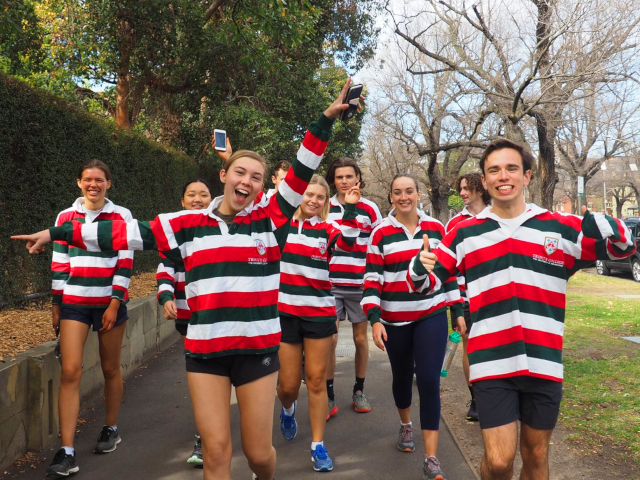 A group of Trinity students wearing their candystripe jumpers walking down the street and smiling.