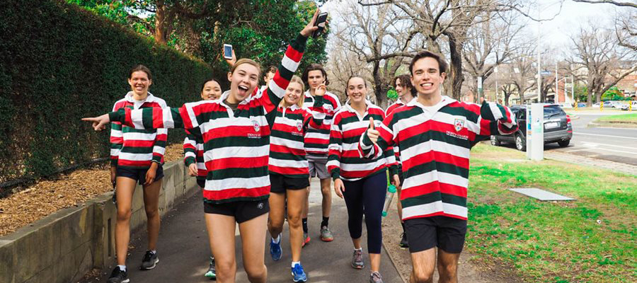A group of Trinity students wearing their candystripe jumpers walking down the street and smiling.