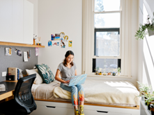 A girl sitting on a bed comfortably in one of Trinity's residential rooms and working on her laptop.