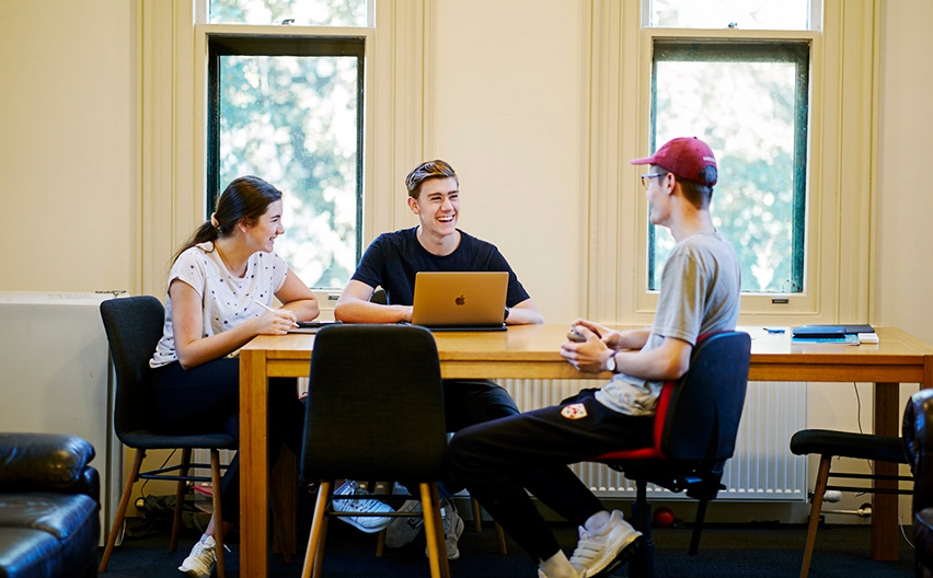 One girl and two boys sitting on the table and talking among themselves with a laptop on the table.