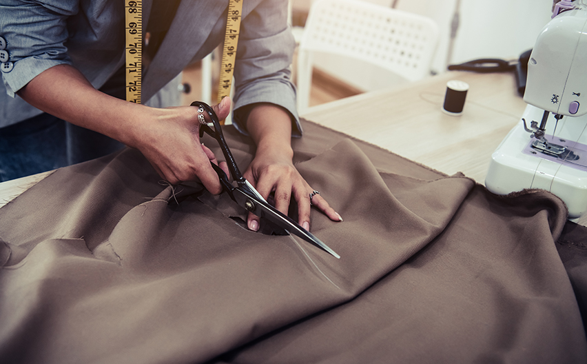 Person cutting fabric with tape measure around their neck