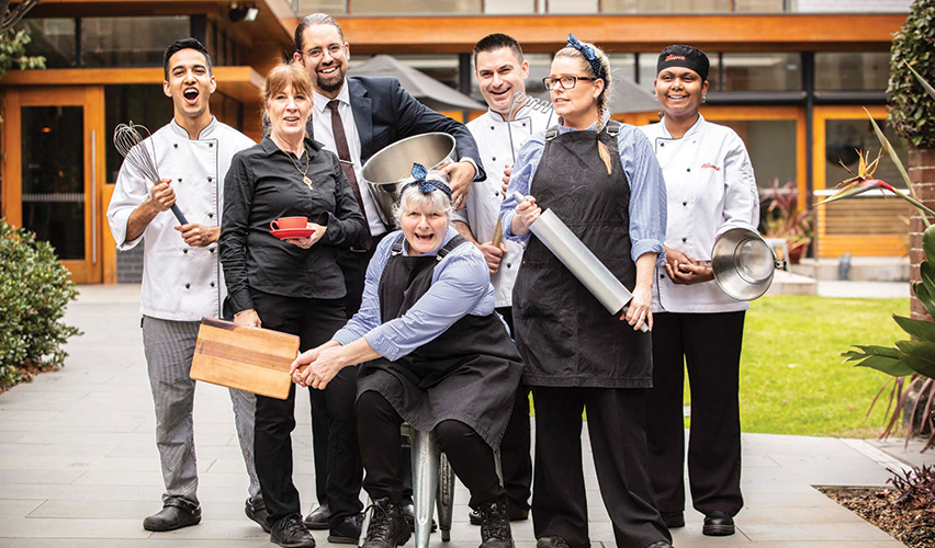 Image of the amazing kitchen team at the residential college posing with all the kitchen tools and having fun.