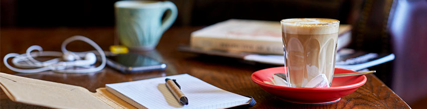 Image of a coffee, an open notebook and pen and some books on the table.
