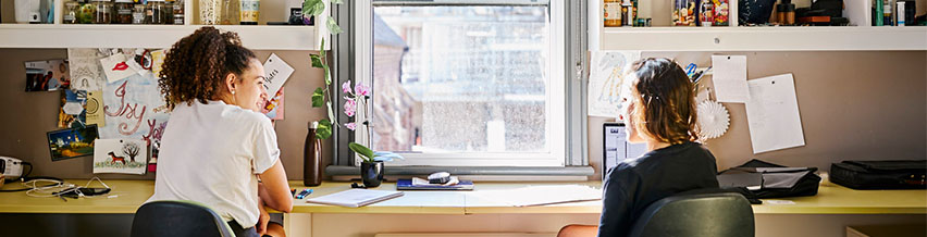 Two girls sitting on the study table in their fully furnished room at our residential college and talking to each other.